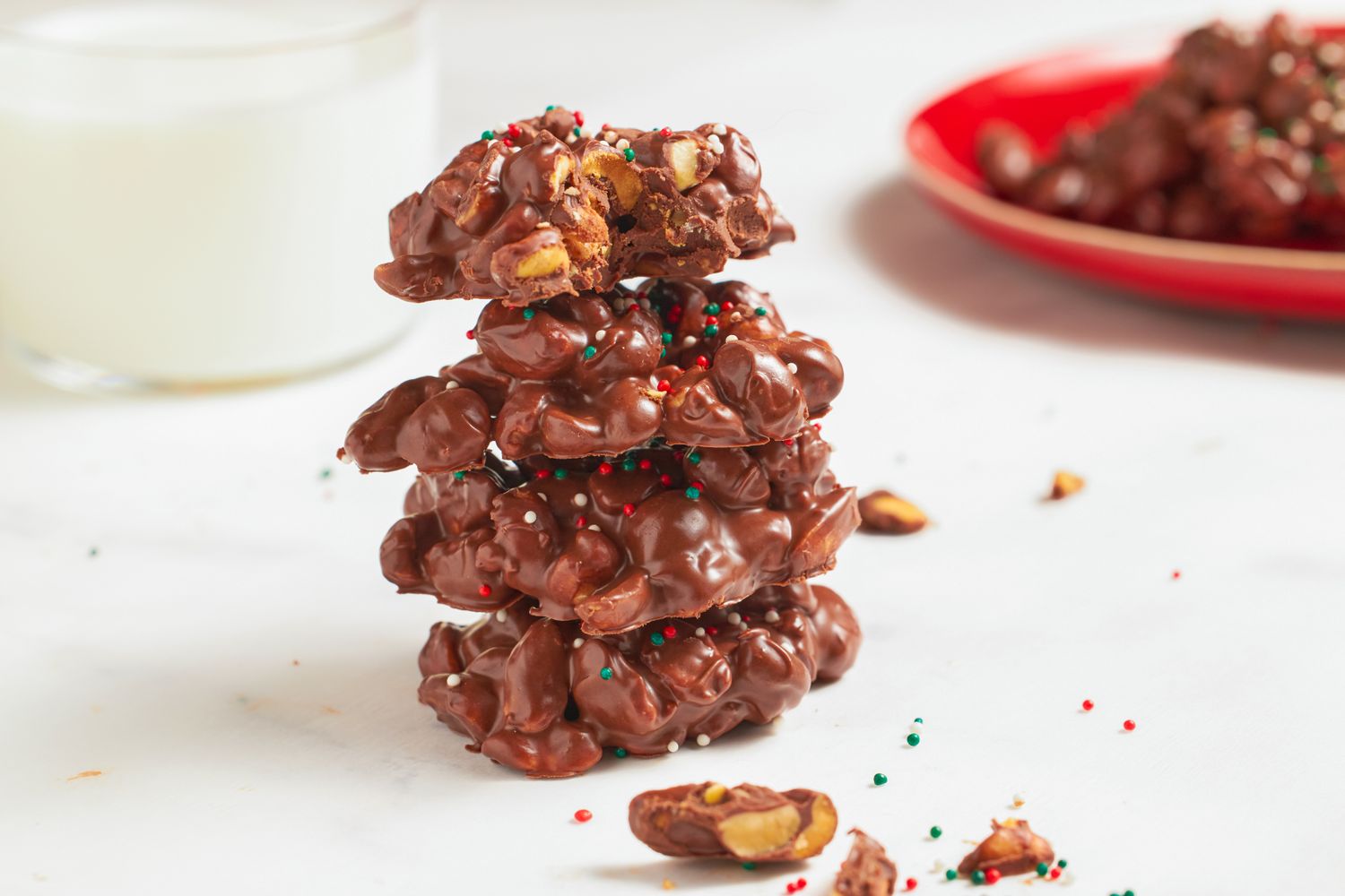 A stack of chocolate clusters with nuts and sprinkles on a white surface