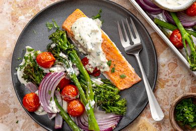Overhead view of a gray plate of salmon, broccolini cherry tomatoes, onions and feta sauce with a fork on a marble countertop