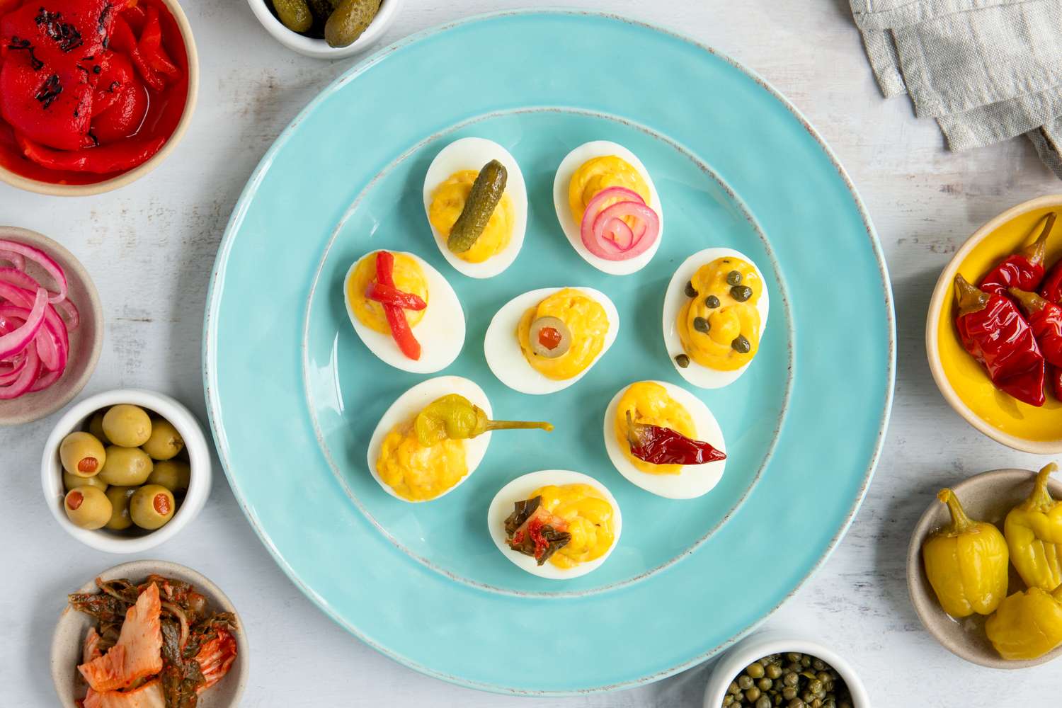 A plate of deviled eggs with various toppings displayed alongside small bowls of garnishes