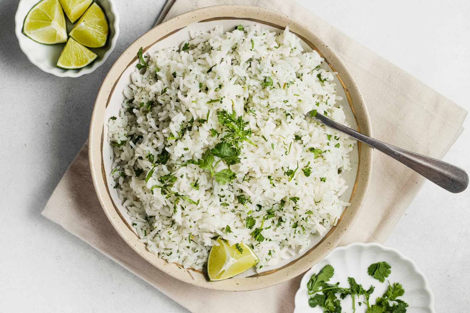 Bowl of Coconut Lime Rice Garnished with Cilantro and Lime Wedge Next to Two Small Bowls (One with Lime Wedges and Another with Cilantro)