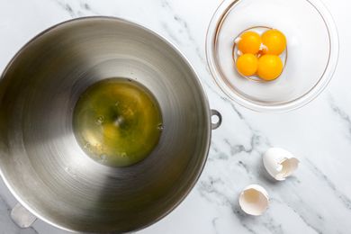 In One Large Bowl, Egg Whites, and Next to It, a Smaller Bowl With Egg Yolks. The Shells on the Counter.