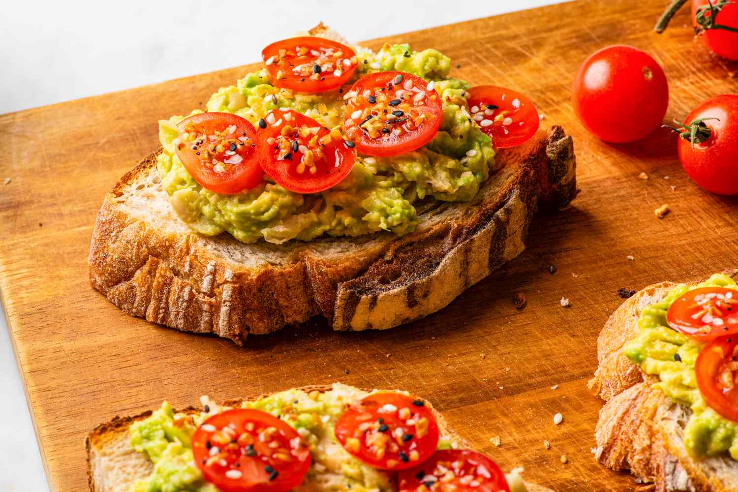 Avocado toast topped with sliced cherry tomatoes and seasoning on a wooden surface