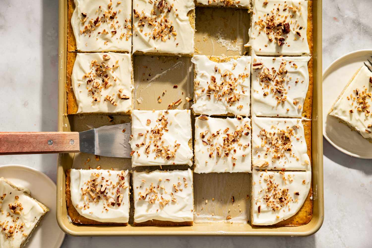 Banana bars topped with frosting and nuts on a baking tray some pieces served on plates