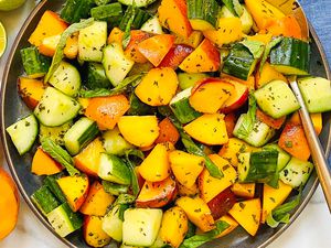 A bowl of peach, cucumber, and basil salad garnished with fresh basil leaves