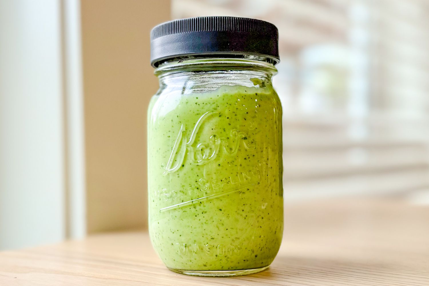 Jar filled with green Duchess dip, placed on a wooden surface near a window.