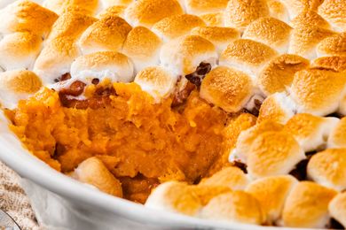 Sweet potato casserole topped with toasted marshmallows partially served in a baking dish