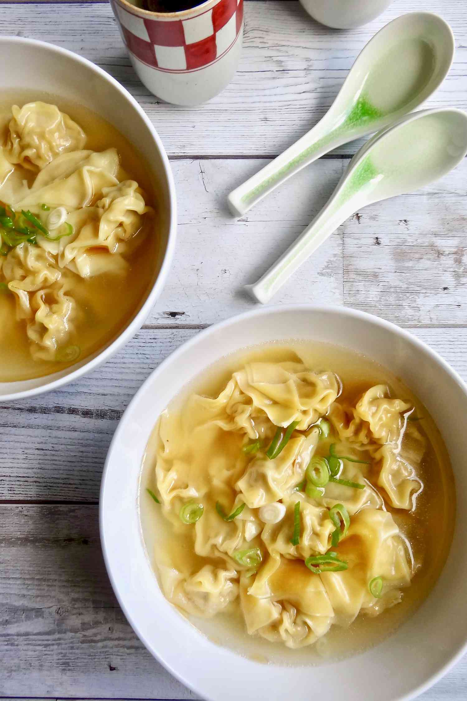Overhead view of a table set with two bowls of easy pork wontons in homemade chicken broth