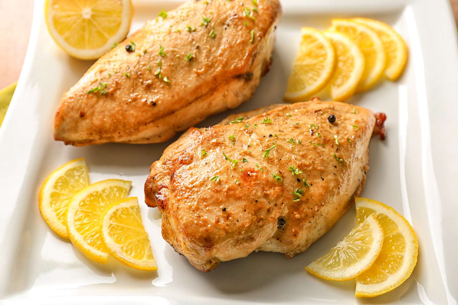 Closeup view of roasted chicken breasts with lemon slices on a white plate