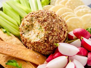 A cheese ball coated in nuts surrounded by crackers radishes celery and other snacks