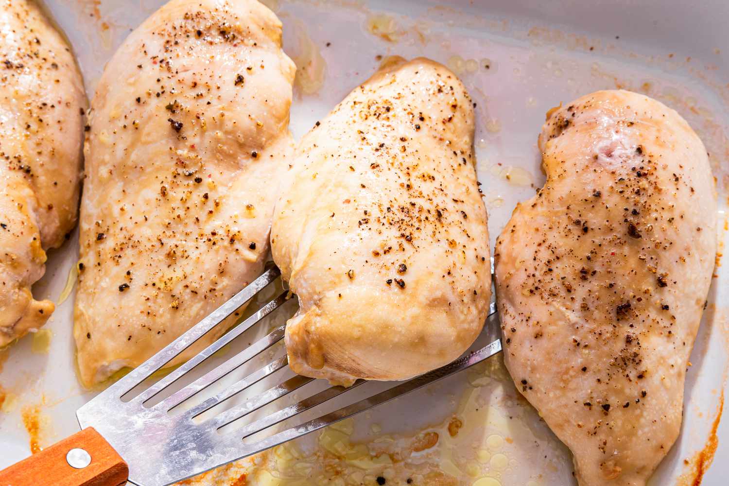 Cooked chicken breast removed from a platter using a spatula 