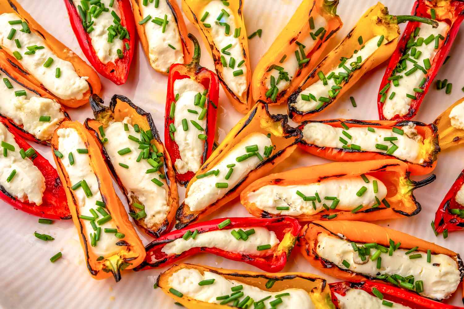 Grilled mini peppers stuffed with feta cheese, garnished with chopped herbs