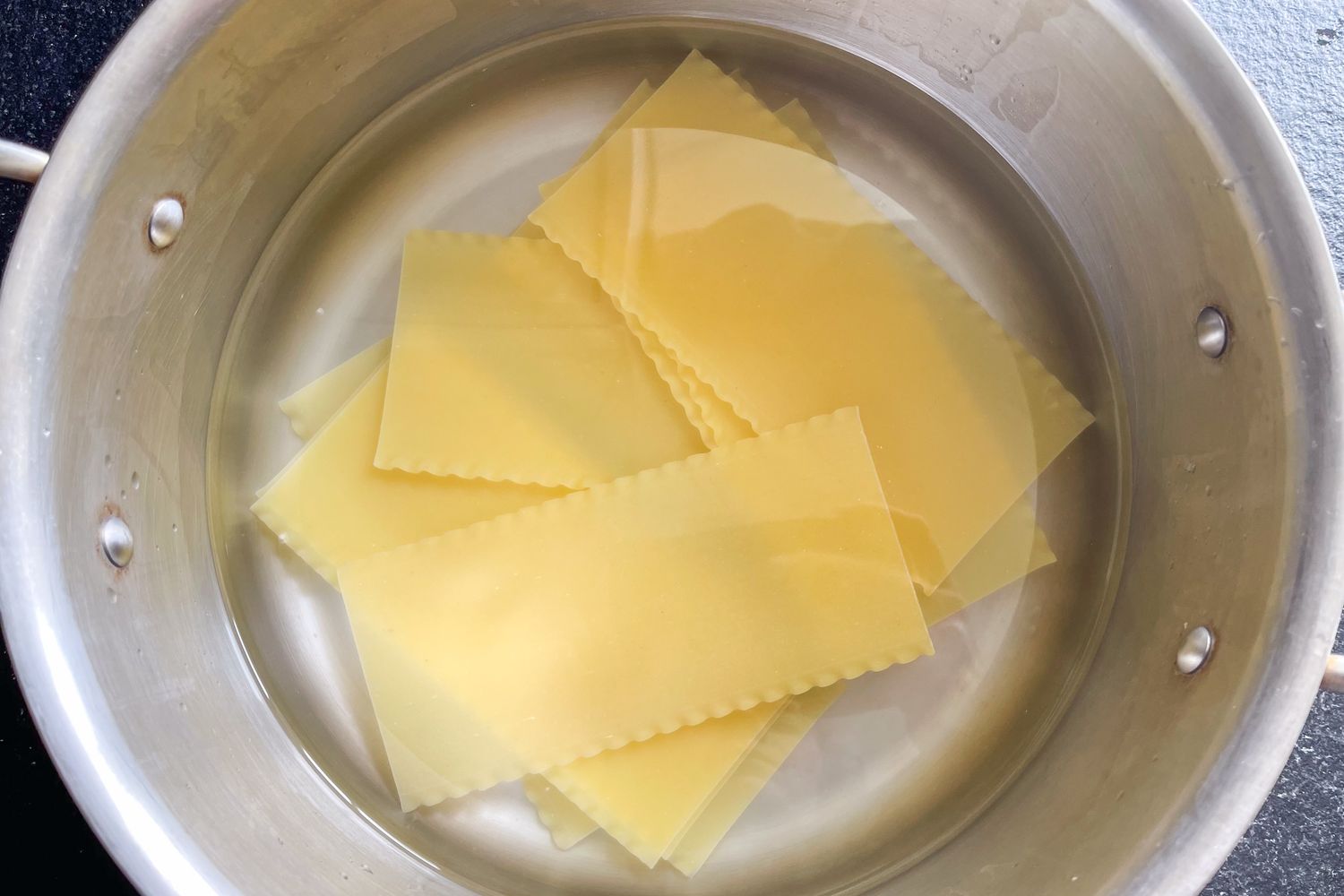 Lasagna noodles soaking in water in a pot