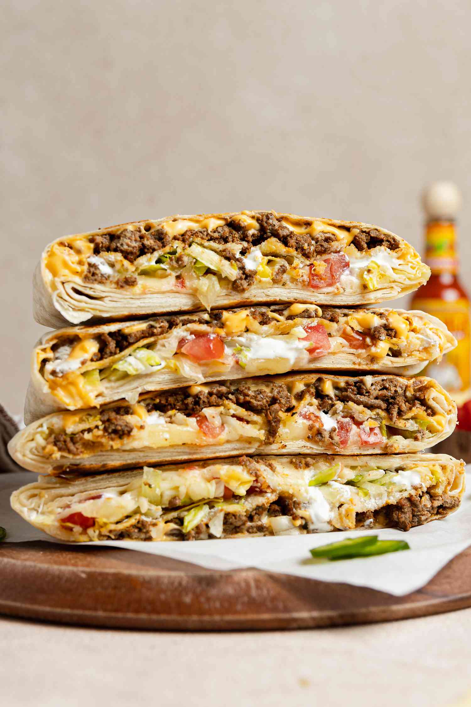 Stack of Copycat Crunchwrap Supreme Cut in Half on Parchment Paper Over a Wooden Board