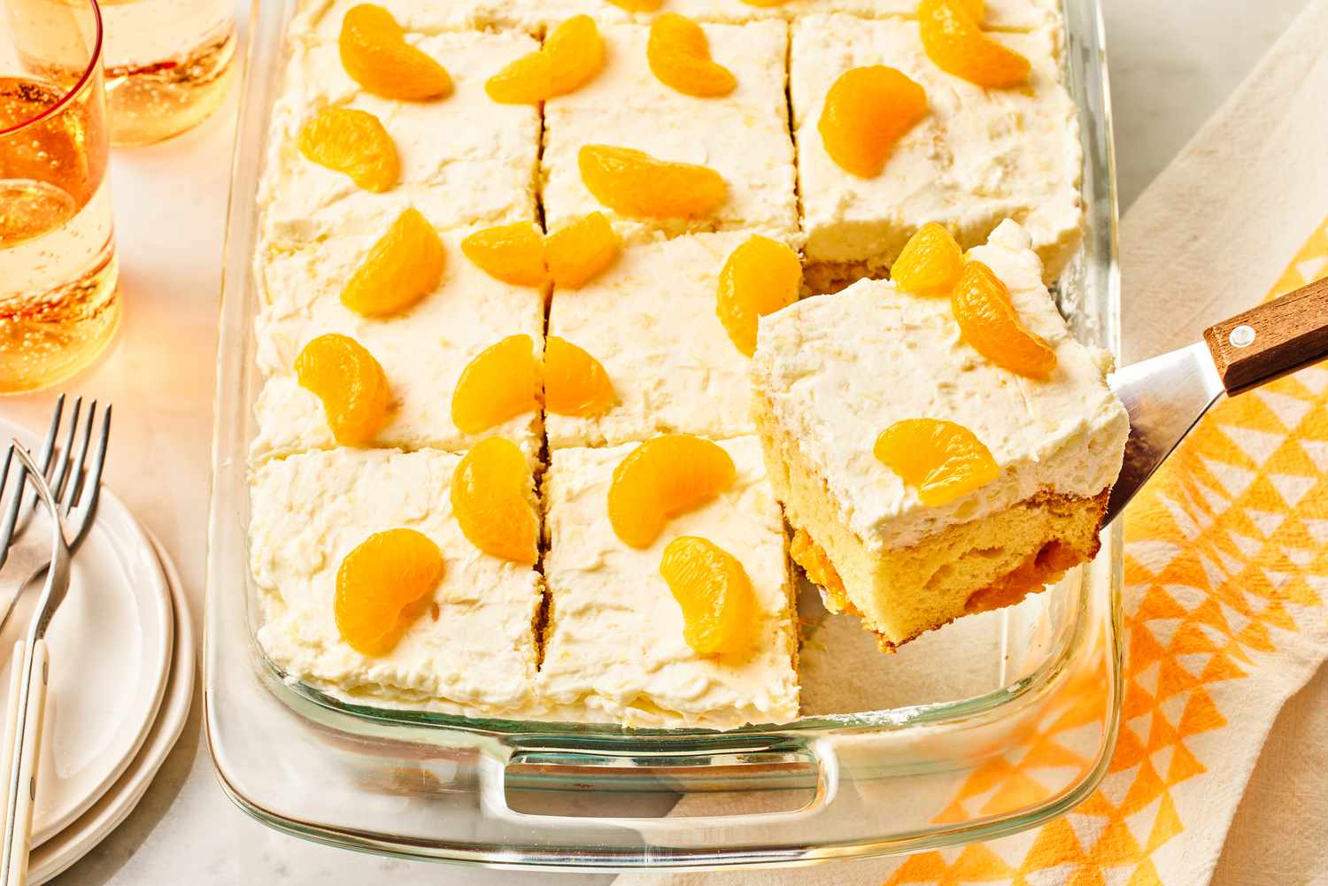 Angled view of a baking dish of pineapple and mandarin orange cake with a slice being removed with a spatula