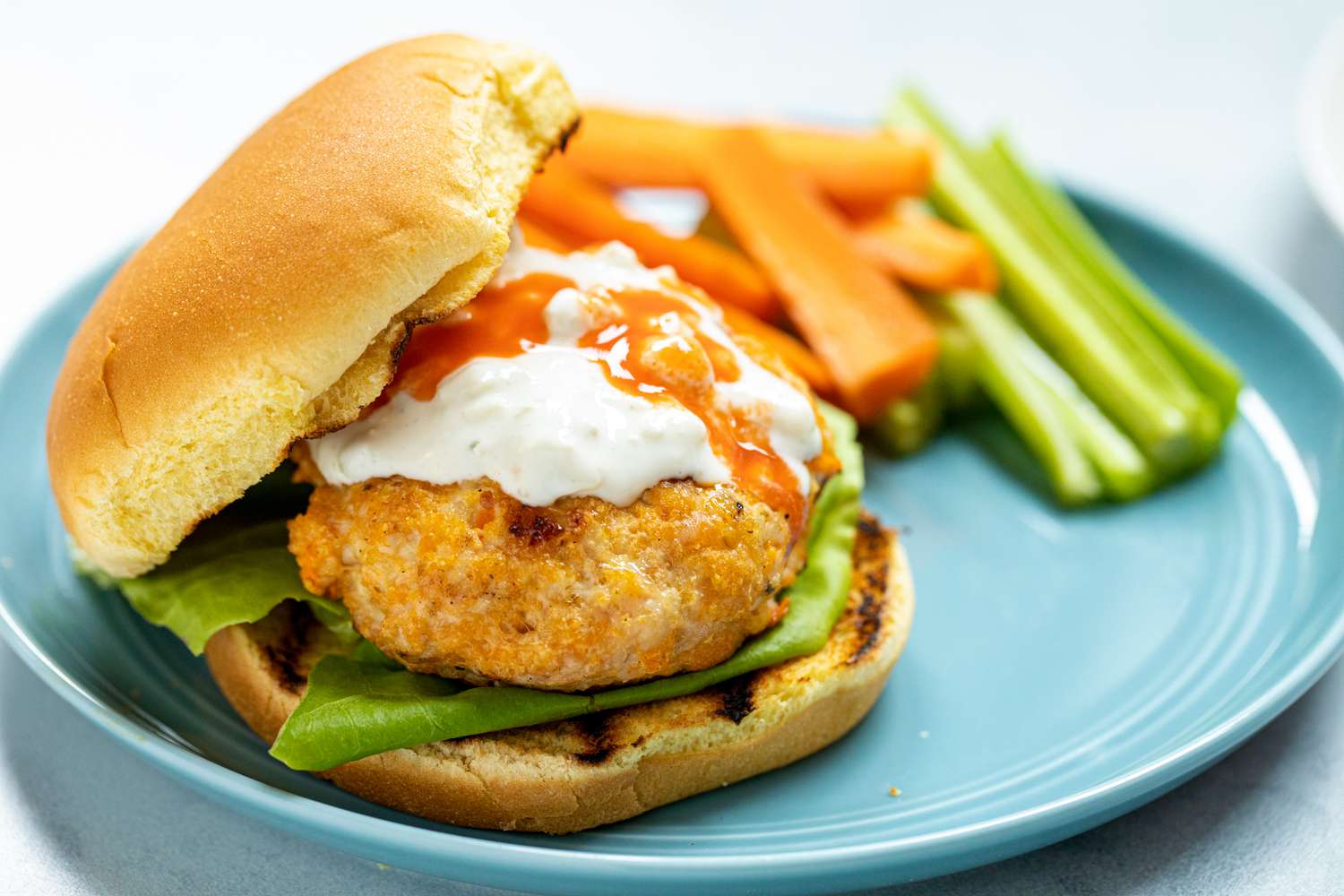 Buffalo chicken burgers with blue cheese sauce on a plate with carrots and celery.