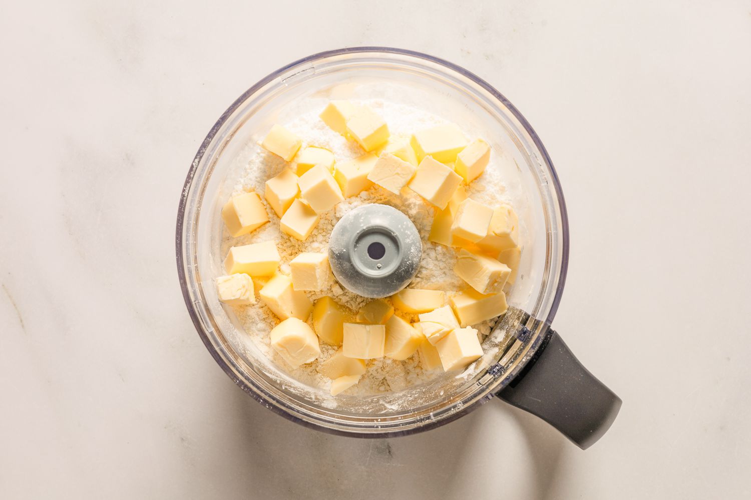 An overhead view of a food processor bowl with the butter and dry ingredients for Sand Tarts recipe