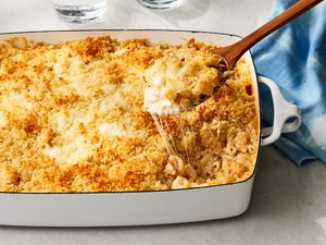 White baking dish of million dollar macaroni and cheese topped with panko with a wooden spoon removing a serving and a blue cloth napkin in the background