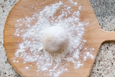Pizza dough ball on a floured wooden pizza peel