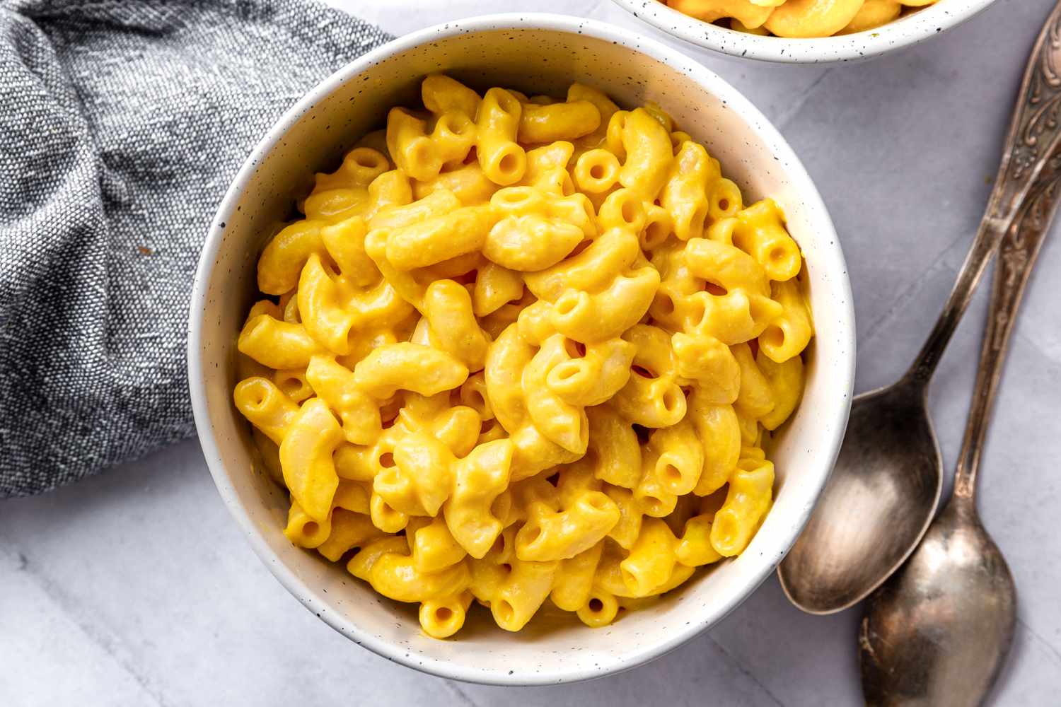Two Bowl of Vegan Mac and Cheese Next to Two Spoons and a Table Napkin