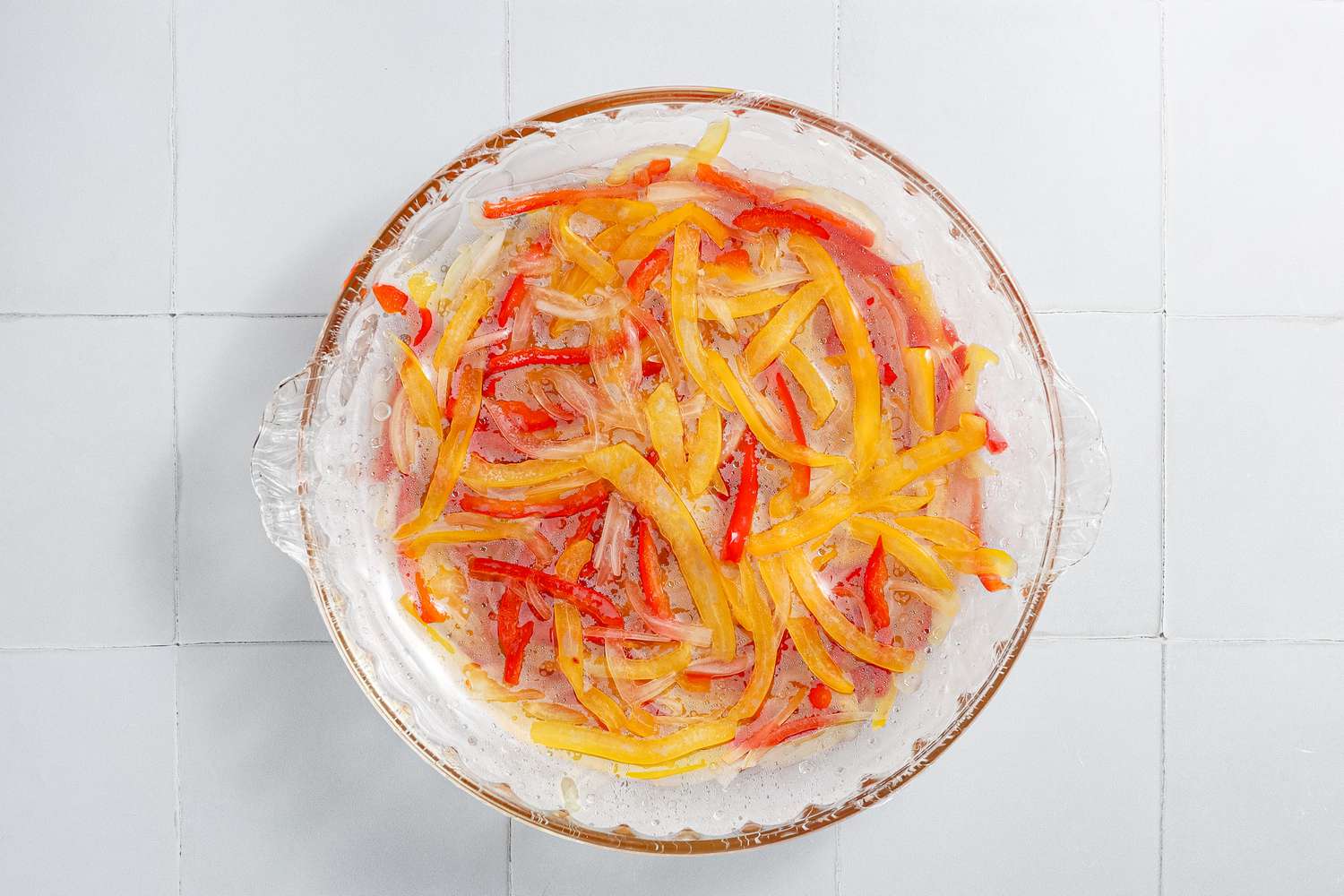 Cooked Sliced Onions and Bell Peppers in a Glass Pyrex Dish Covered in Plastic Wrap for Microwave Shakshuka Recipe 