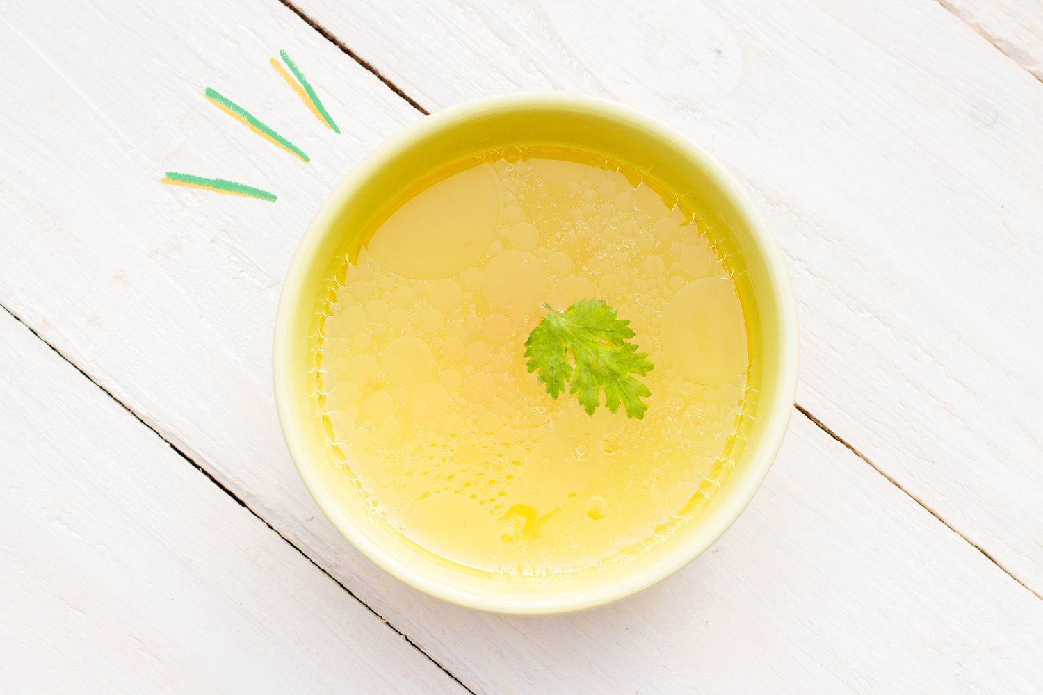 A bowl of chicken broth with a leaf garnish on a wooden surface
