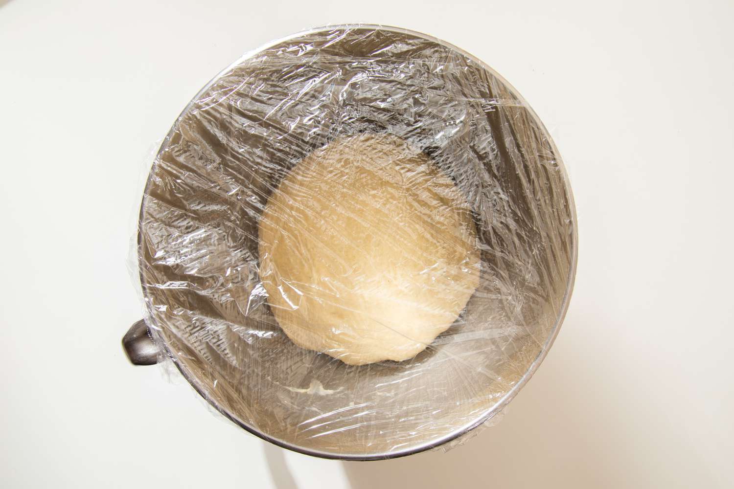 Salted honey rolls dough resting in a mixer bowl covered in plastic wrap
