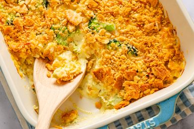 Casserole dish with chicken divan topped with crushed crackers a wooden spoon serving a portion
