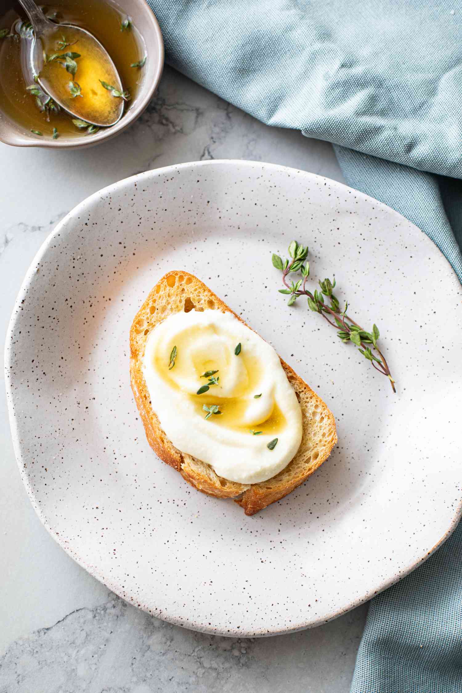 Two Pieces of Whipped Ricotta Toast Topped with Lemon-Thyme Honey Next to a Bowl of Honey