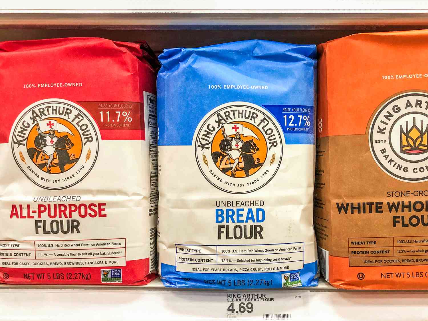 Bags of King Arthur brand flour on a store shelf, displaying different types such as all-purpose, bread, and whole wheat