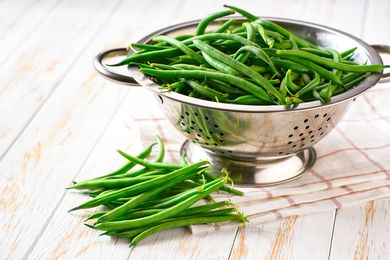 Side view of green beans in a colander on a white table