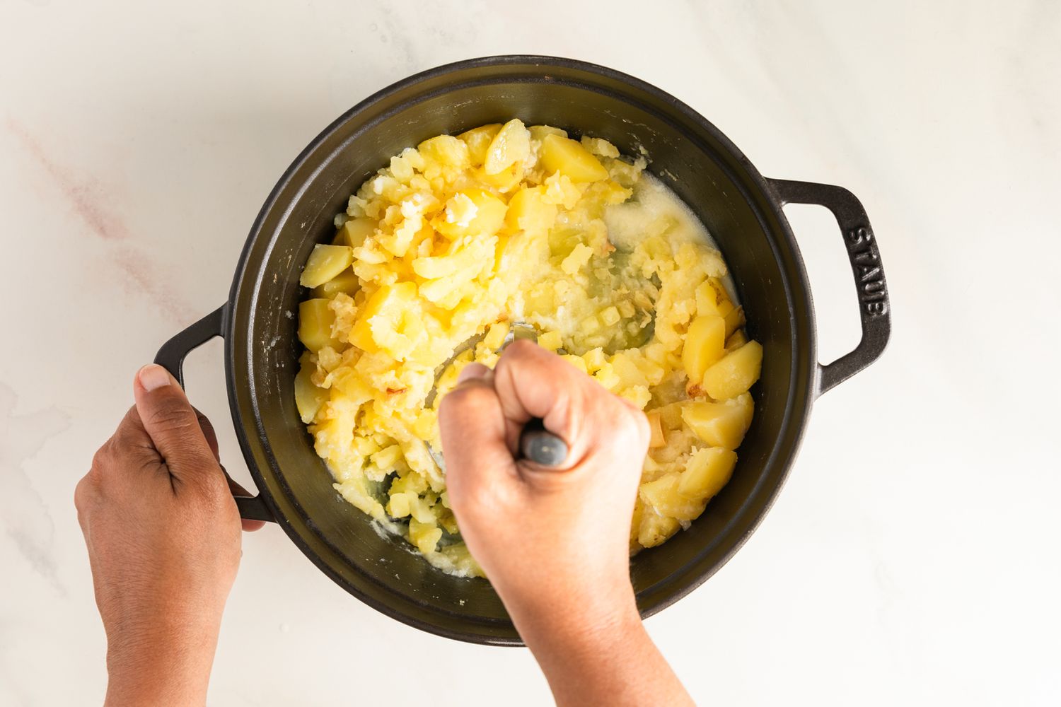 Mashing the cooked potatoes and garlic with a potato masher