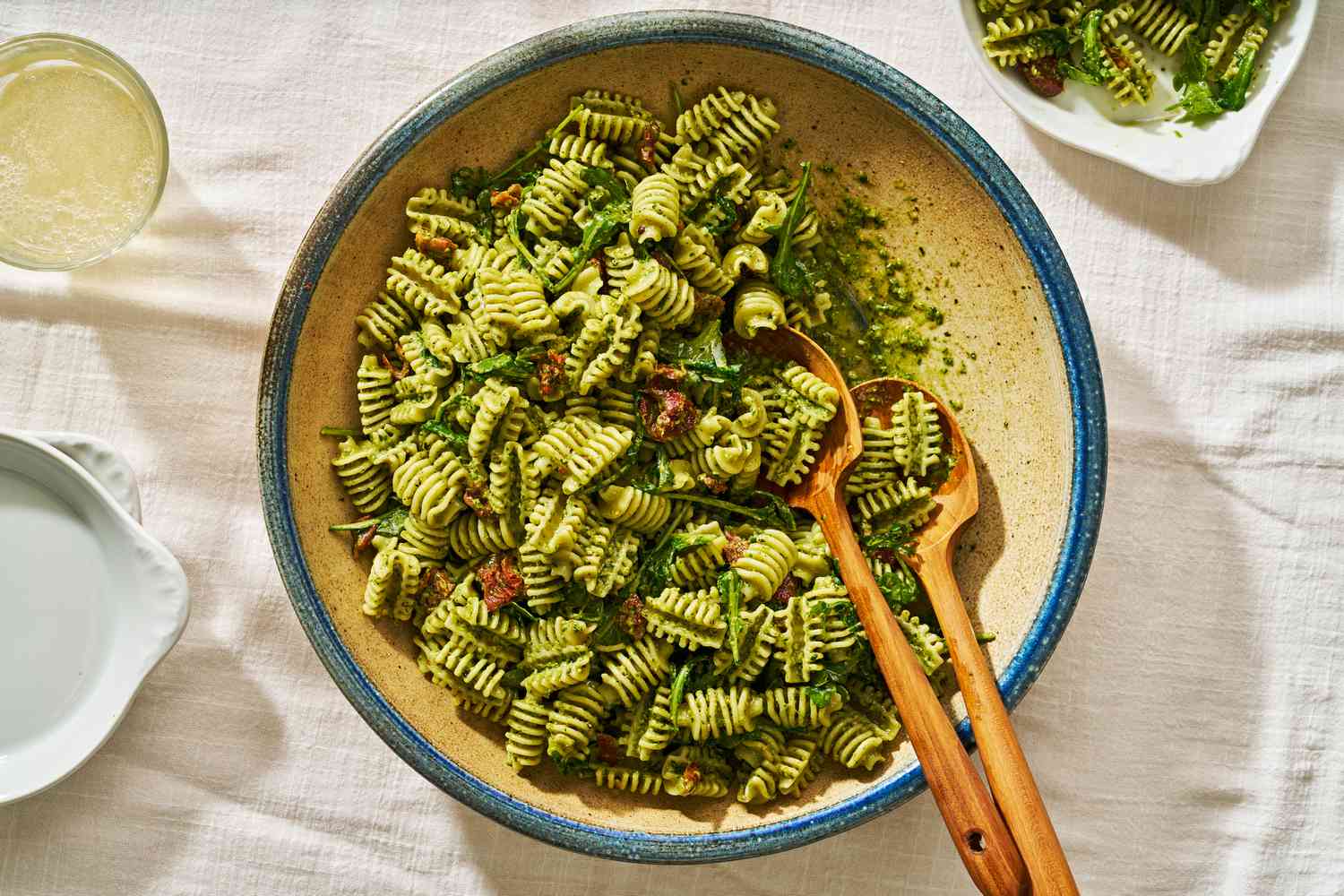 5-ingredient pesto pasta salad in a big bowl next to a glass of lemonade, a serving of pasta salad on a plate, and a stack of plates