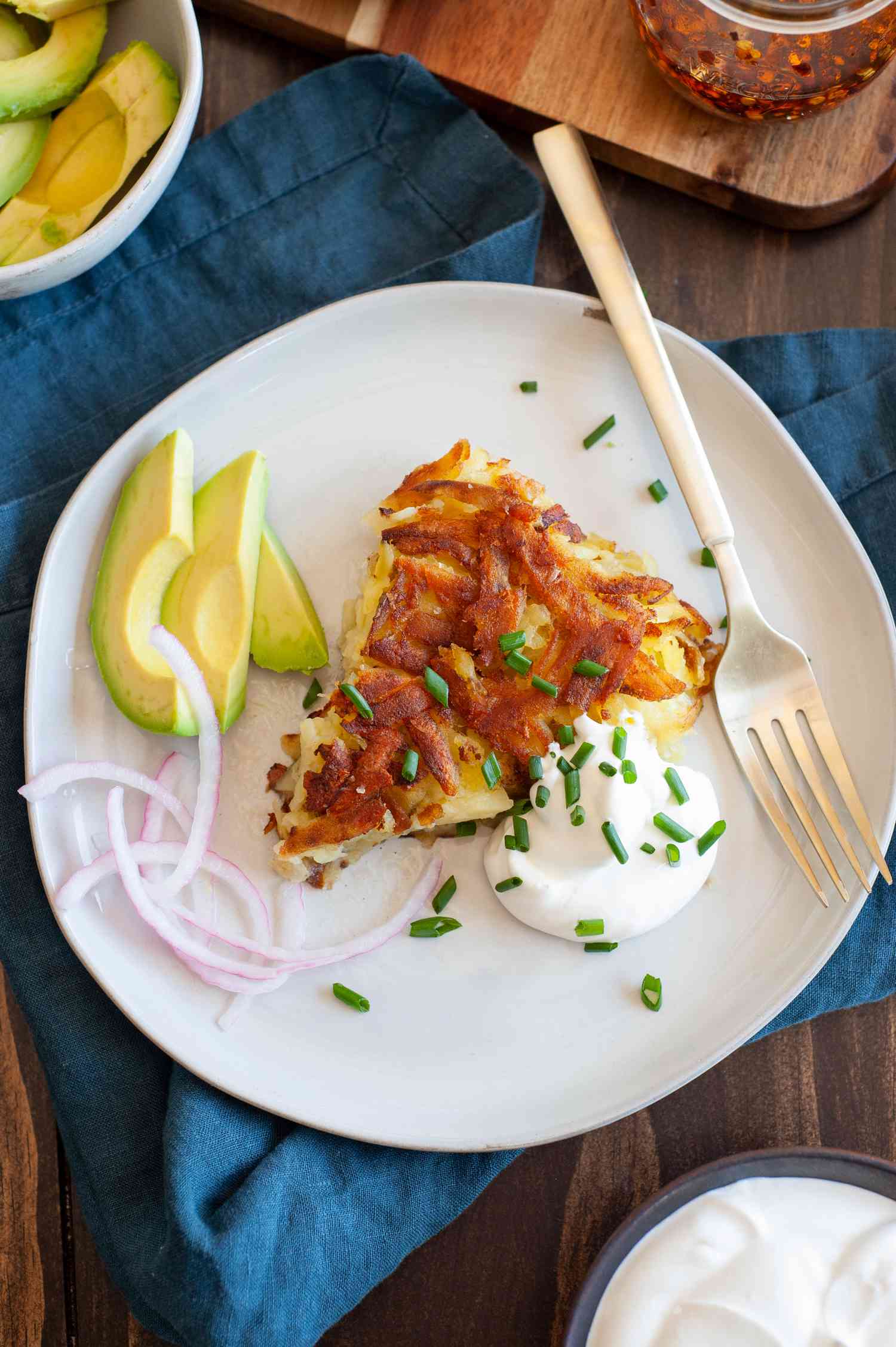 Slice of Rosti on a Plate with Sour Cream, Sliced Avocados, and Sliced Onions