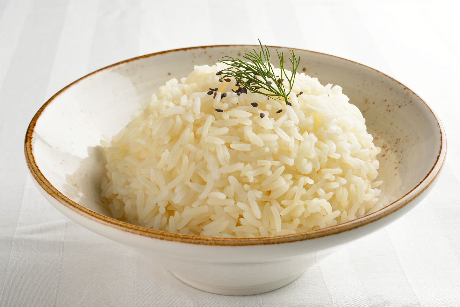A bowl of cooked jasmine rice garnished with sesame seeds and a sprig of dill