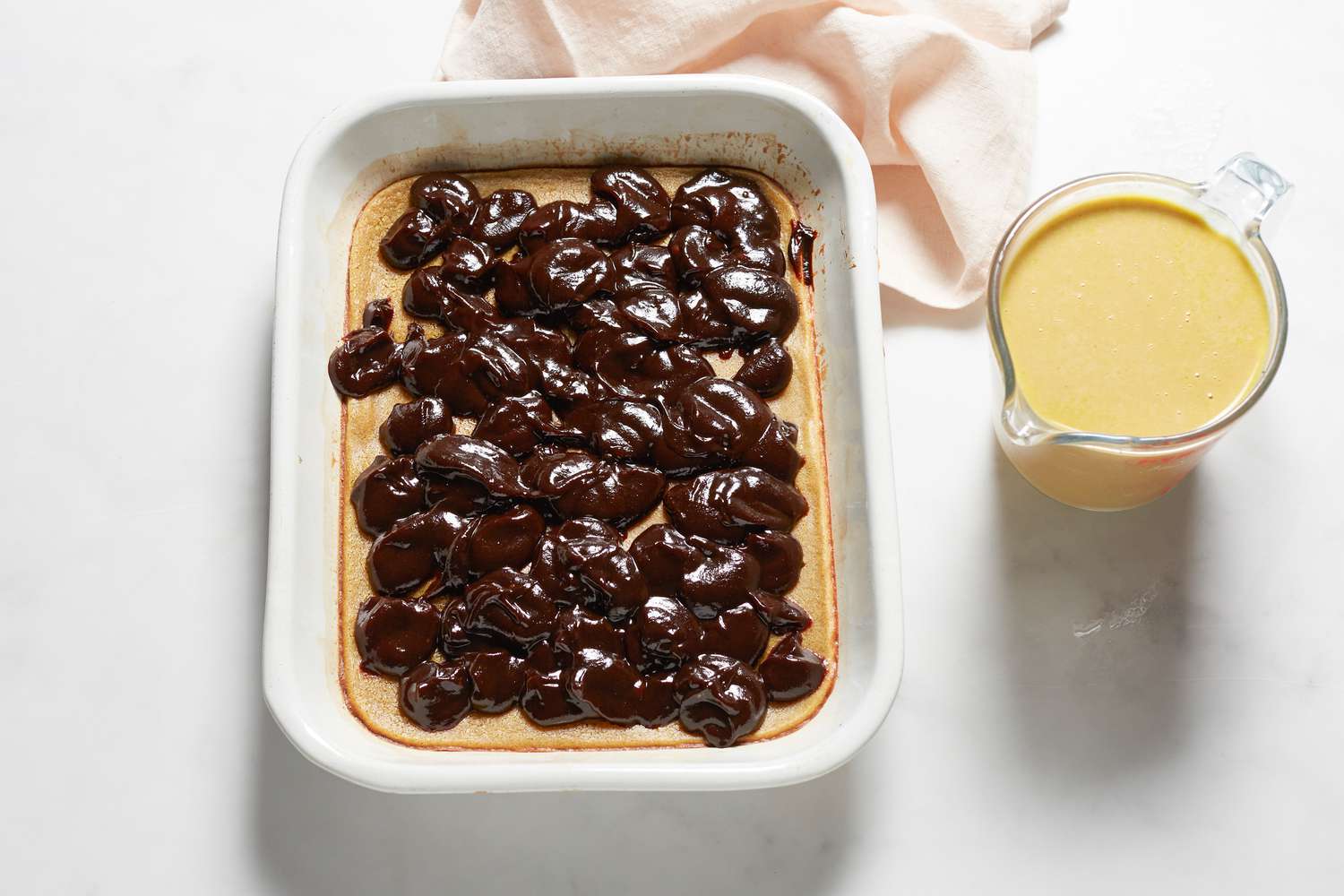 Pouring batter and spreading bean paste on a Sticky rice cake with red bean paste in a baking dish.