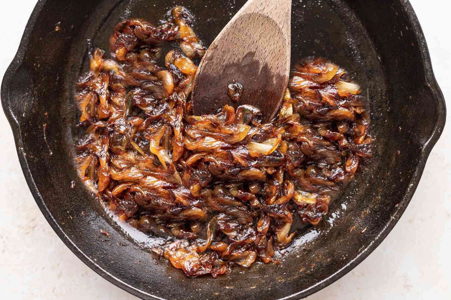 A wooden spoon stirring caramelized onions in a cast iron skillet to show how to make caramelized onions.