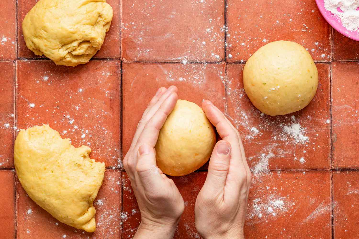Hand shaping a dough portion into a ball for pan de muerto recipe 