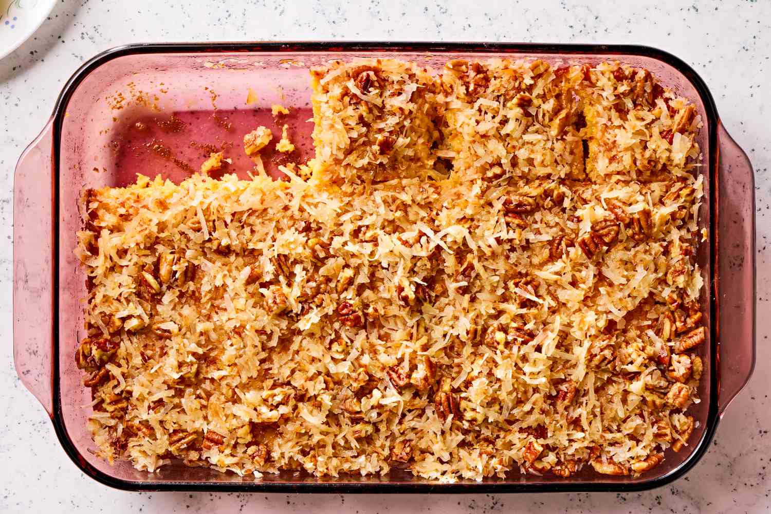 Overhead view of a glass baking dish of pineapple coconut cake with two slices removed