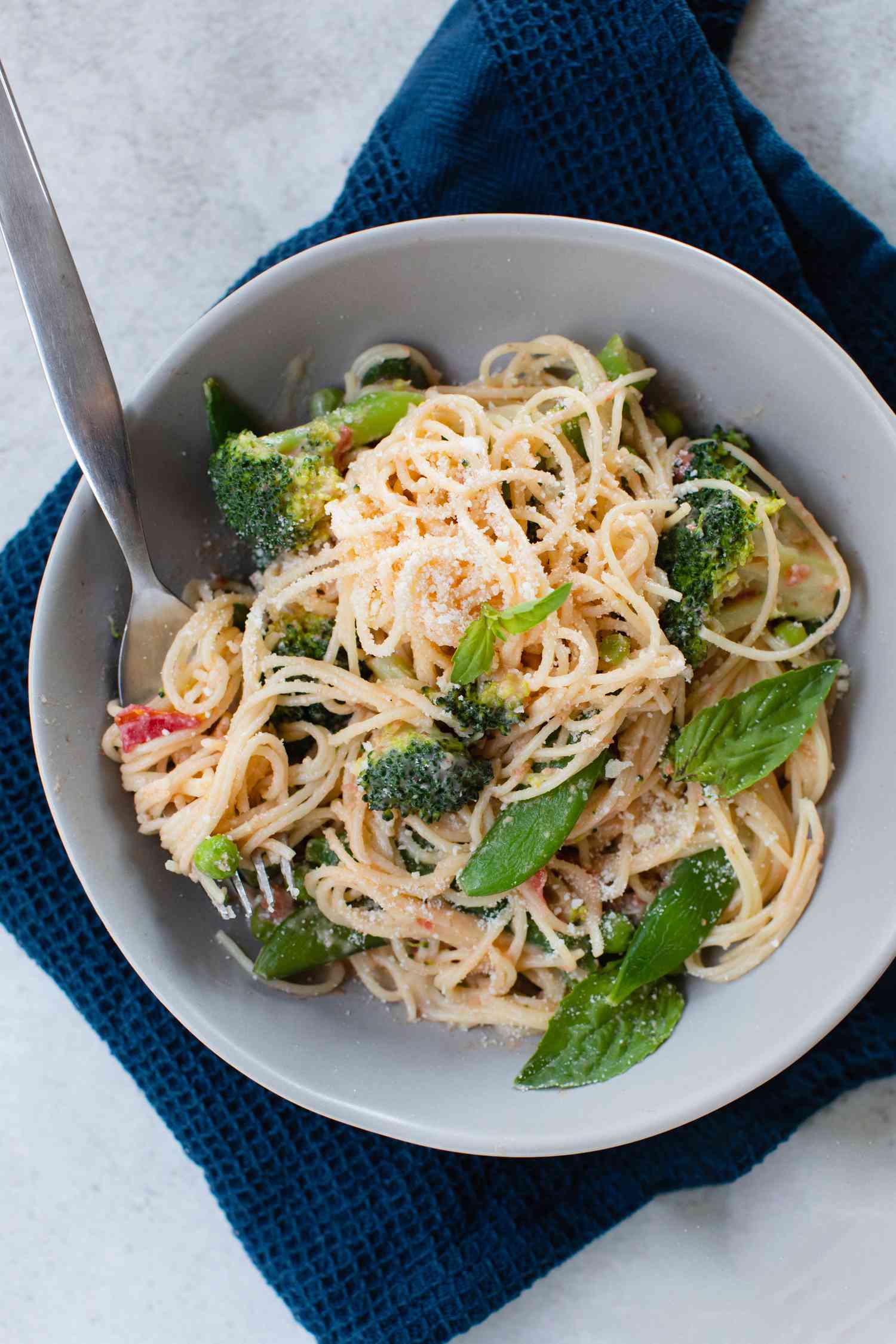 Overhead view of primavera pasta in a bowl with a navy linen underneath.