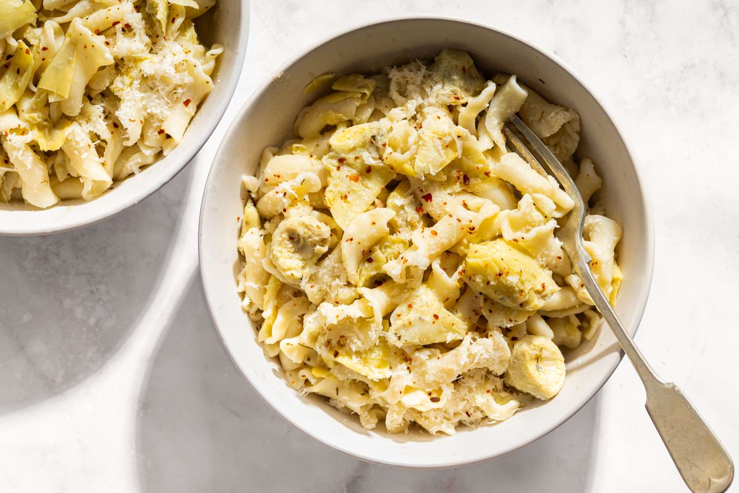 A bowl of pasta with artichokes and lemon garnished with a sprinkle of seasoning and a fork in the bowl
