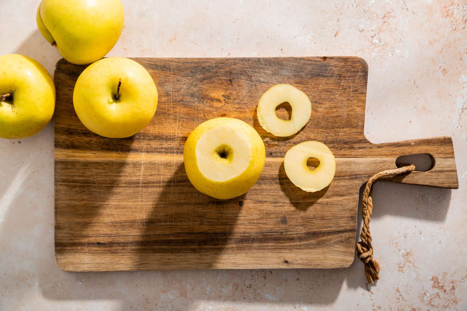 A wooden cutting board with whole and cored apples arranged alongside a few apple slices