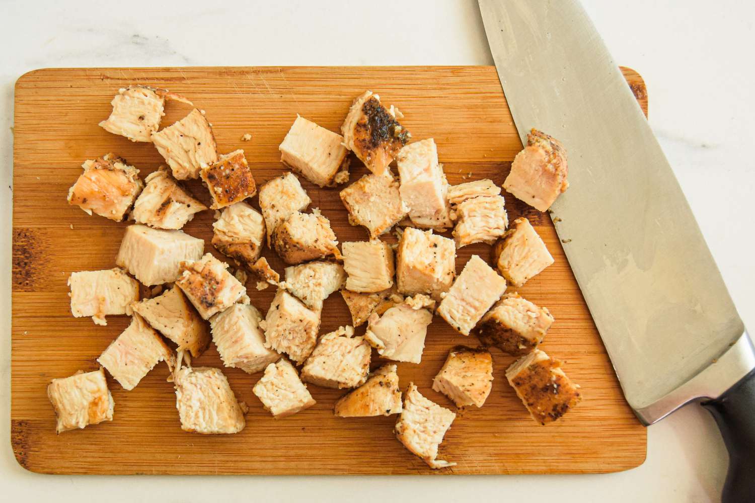 Cooked Chicken Breast Cut Into Bite Size Pieces on a Cutting Board for Alfredo Pizza Recipe