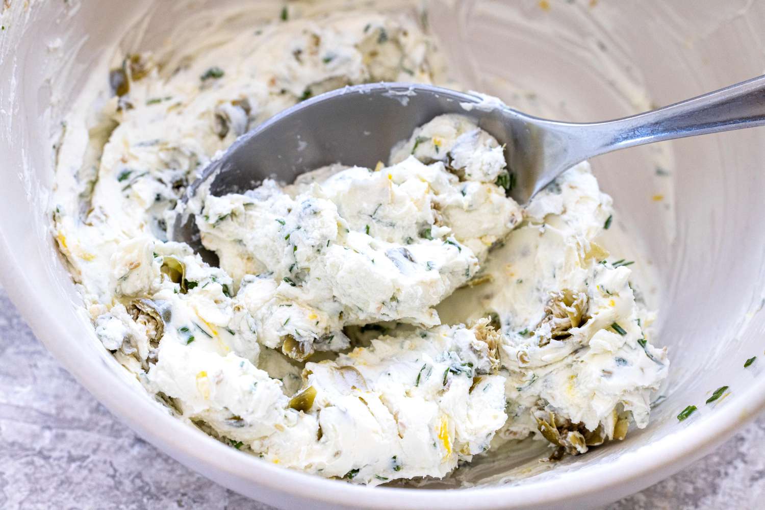 Mixing the cream cheese spread in a bowl to make smoked salmon, cucumber, and cream cheese crostini.