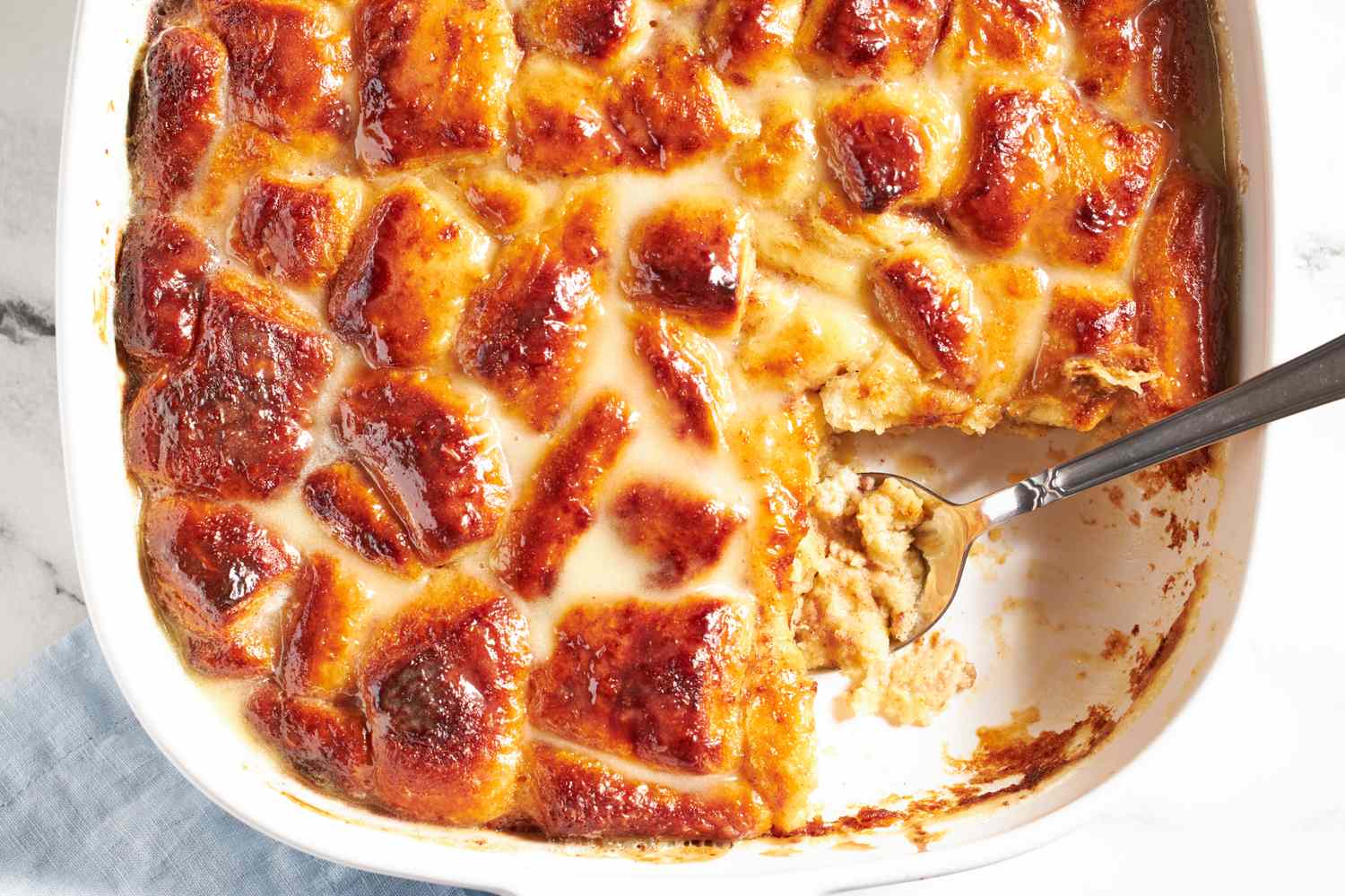 A baked dish of cinnamon roll bread pudding served with a spoon