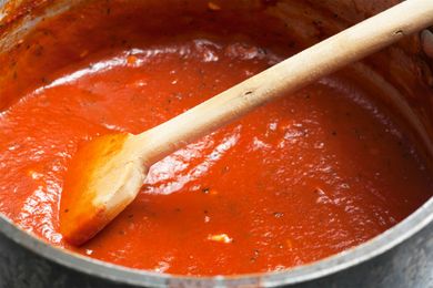 A pot of tomato sauce being stirred with a wooden spoon featured in a reciperelated context