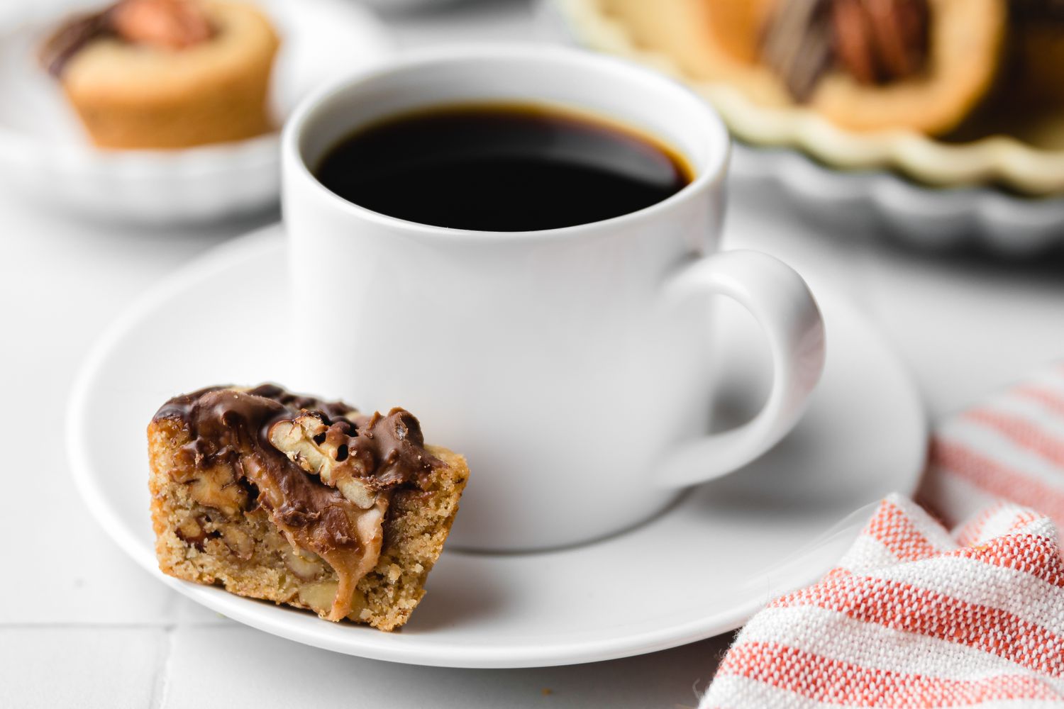 Halved Turtle Cookie Cup on a Saucer Next to a Cup of Coffee, and in the Background, More on a Plate and on Another Saucer