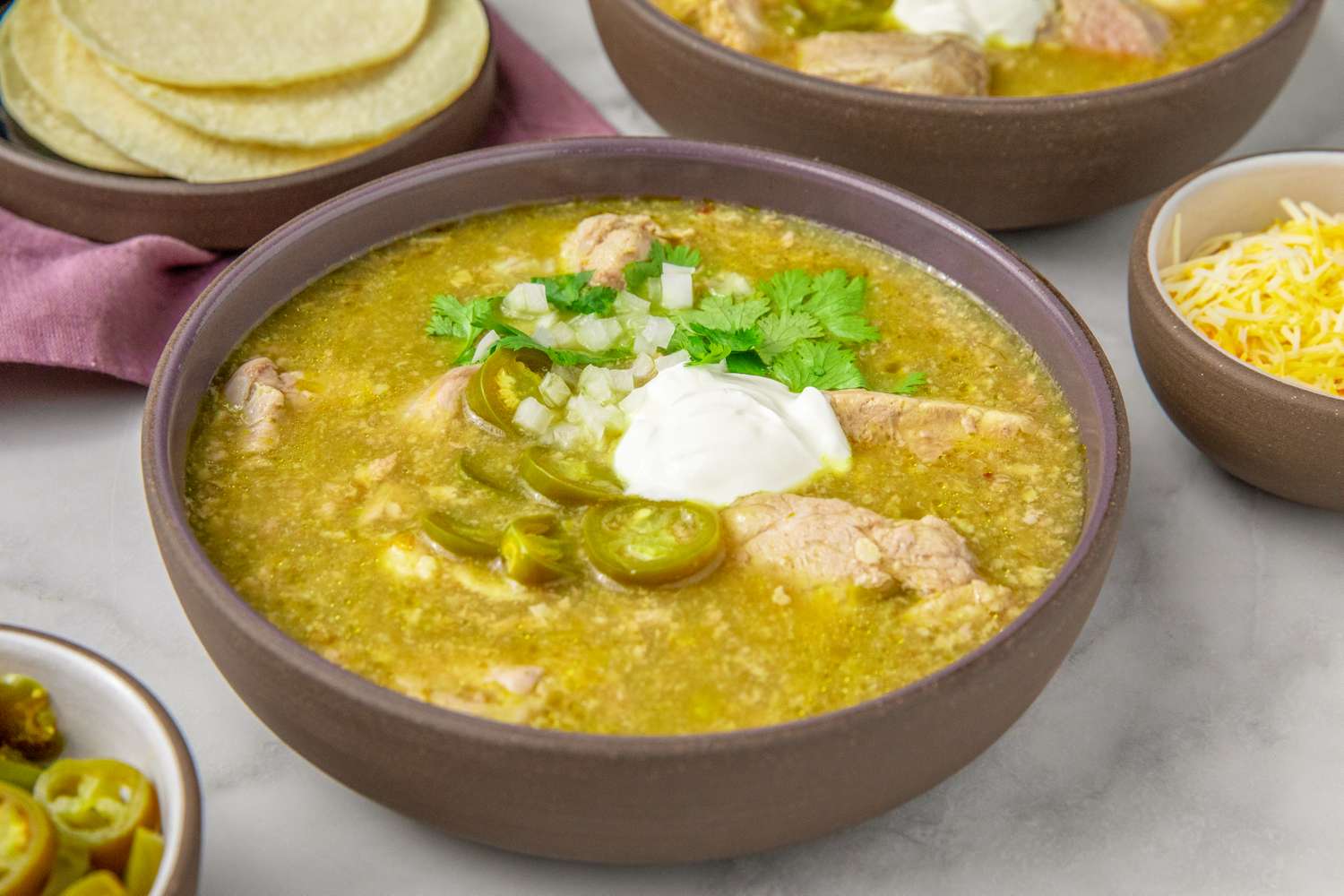 Bowl of pork chile verde garnished with sour cream cilantro and jalapeos