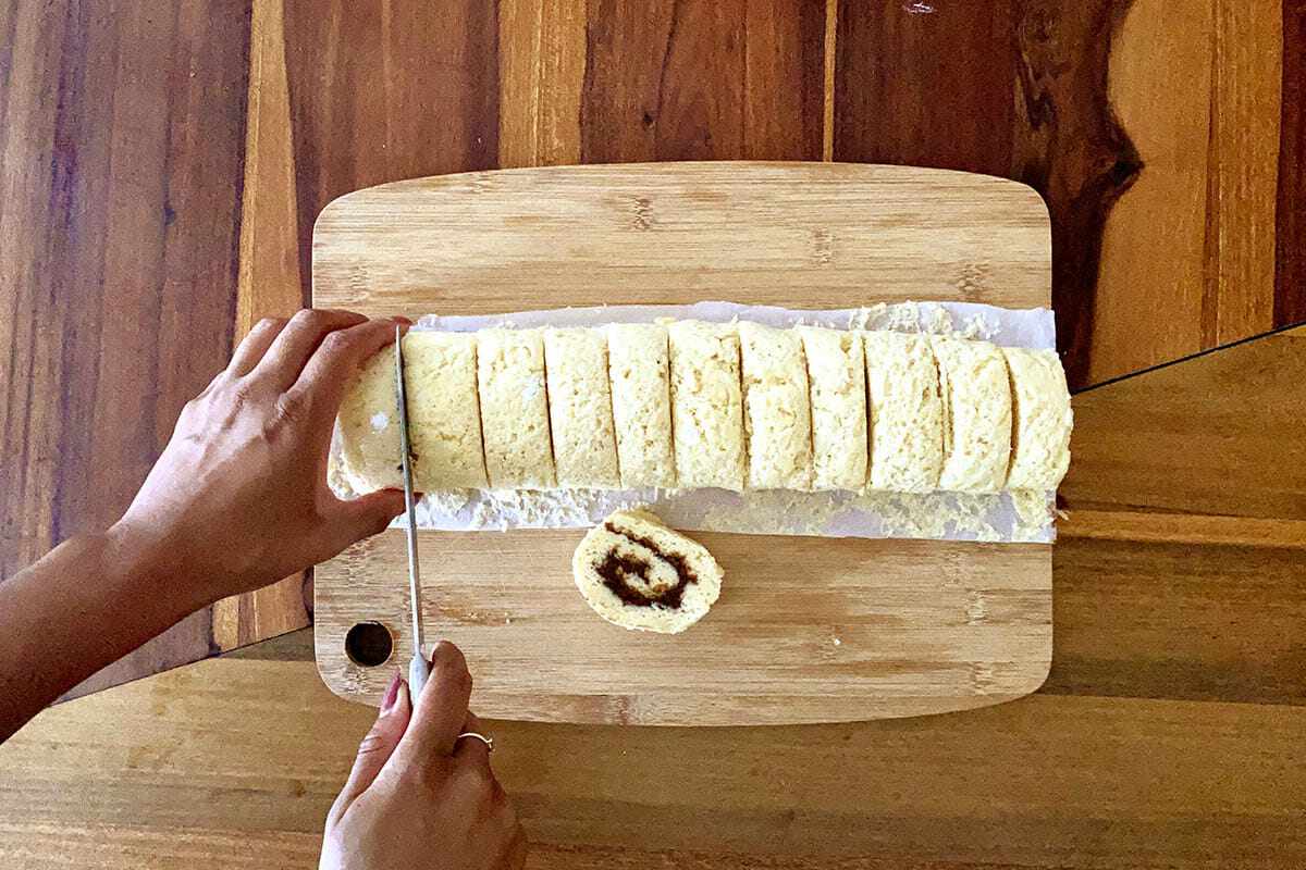 Rolls being sliced on a cutting board to show how to make gluten free cinnamon rolls.