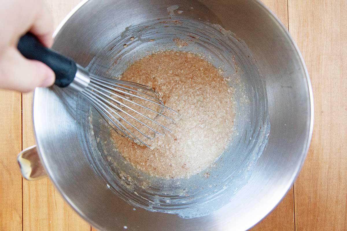 A whisk is mixing ingredients in a metal bowl for a homemade king cake.