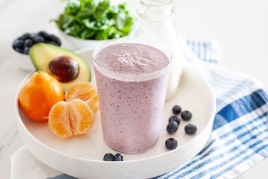 Blueberry breakfast smoothie on a tray along with fresh fruit and vegetables.